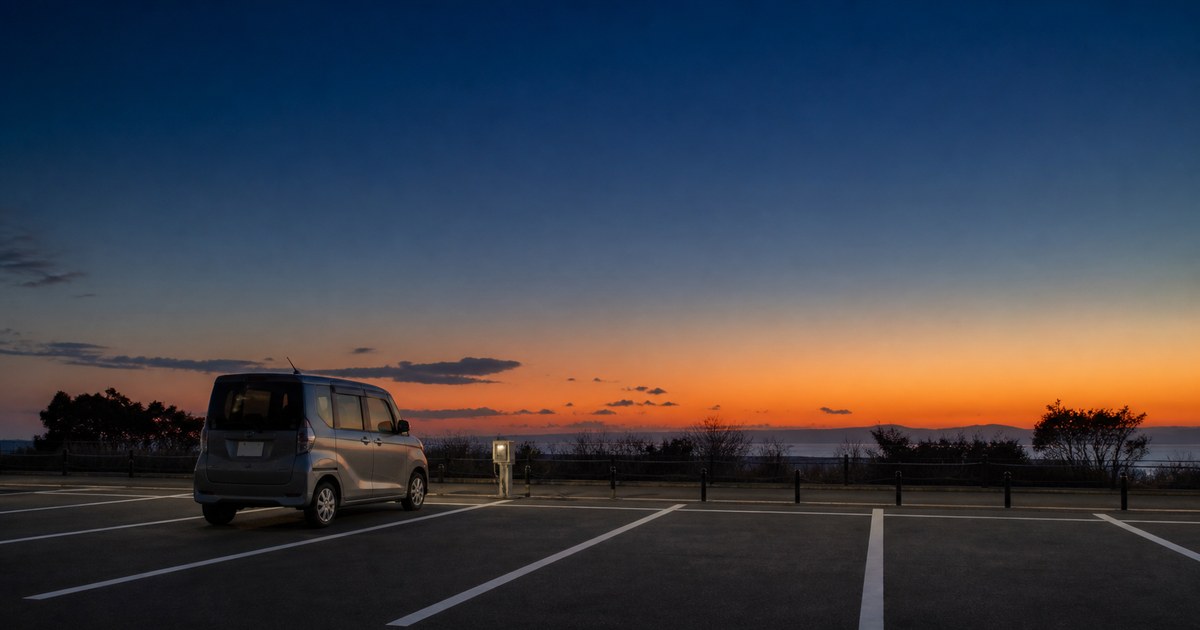 夕暮れの区画された駐車スペースに停まった軽自動車と電源ボックス。RVパークのイメージ