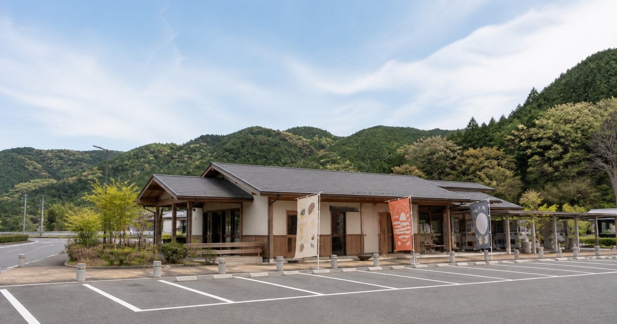 山あいの一般道沿いに建つ道の駅の全景。平屋の建物とのぼり旗、広い駐車場